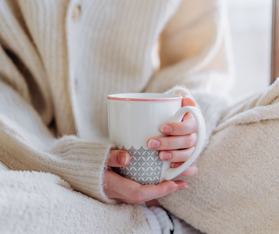 Close-up of a woman in a cozy sweater holding a warm mug on her lap—perfectly capturing the calm of a slow, cozy fall morning routine.