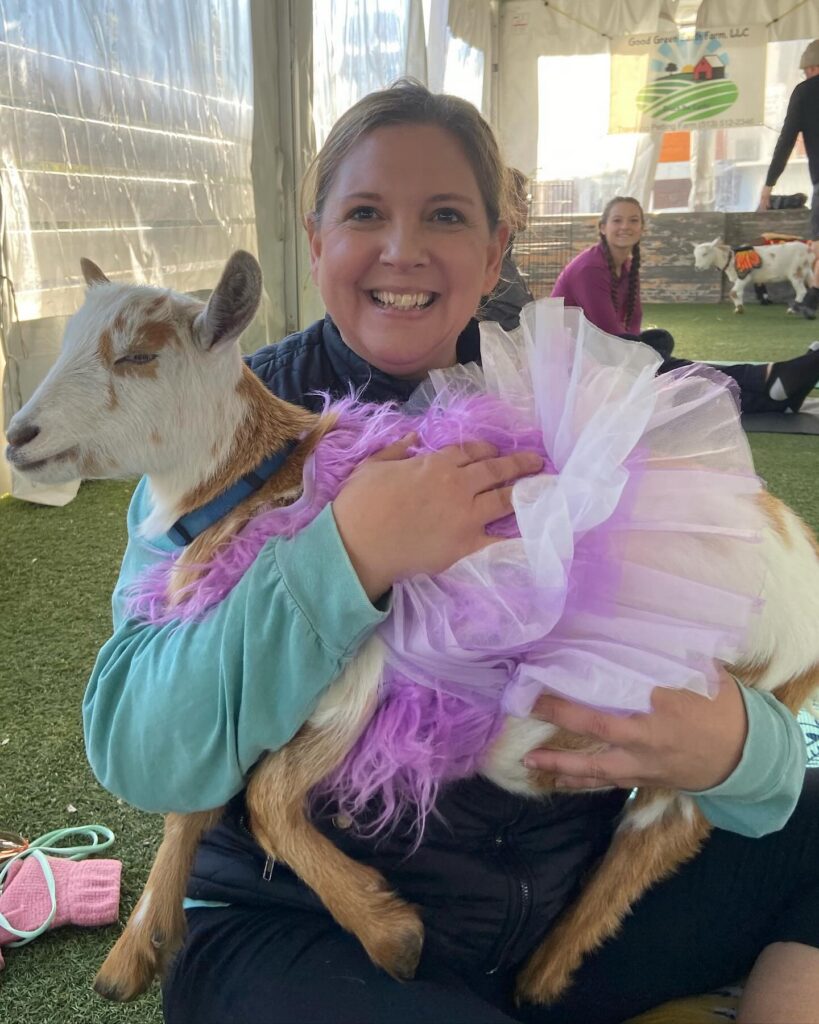 Tara smiling while holding a goat in a tutu during goat yoga—rediscovering joy in midlife.